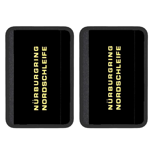 Two black neoprene seat belt cover pads with 'Nürburgring Nordschleife' text in yellow, indicating a racing track, suggesting the product is designed for use in car seat belts.