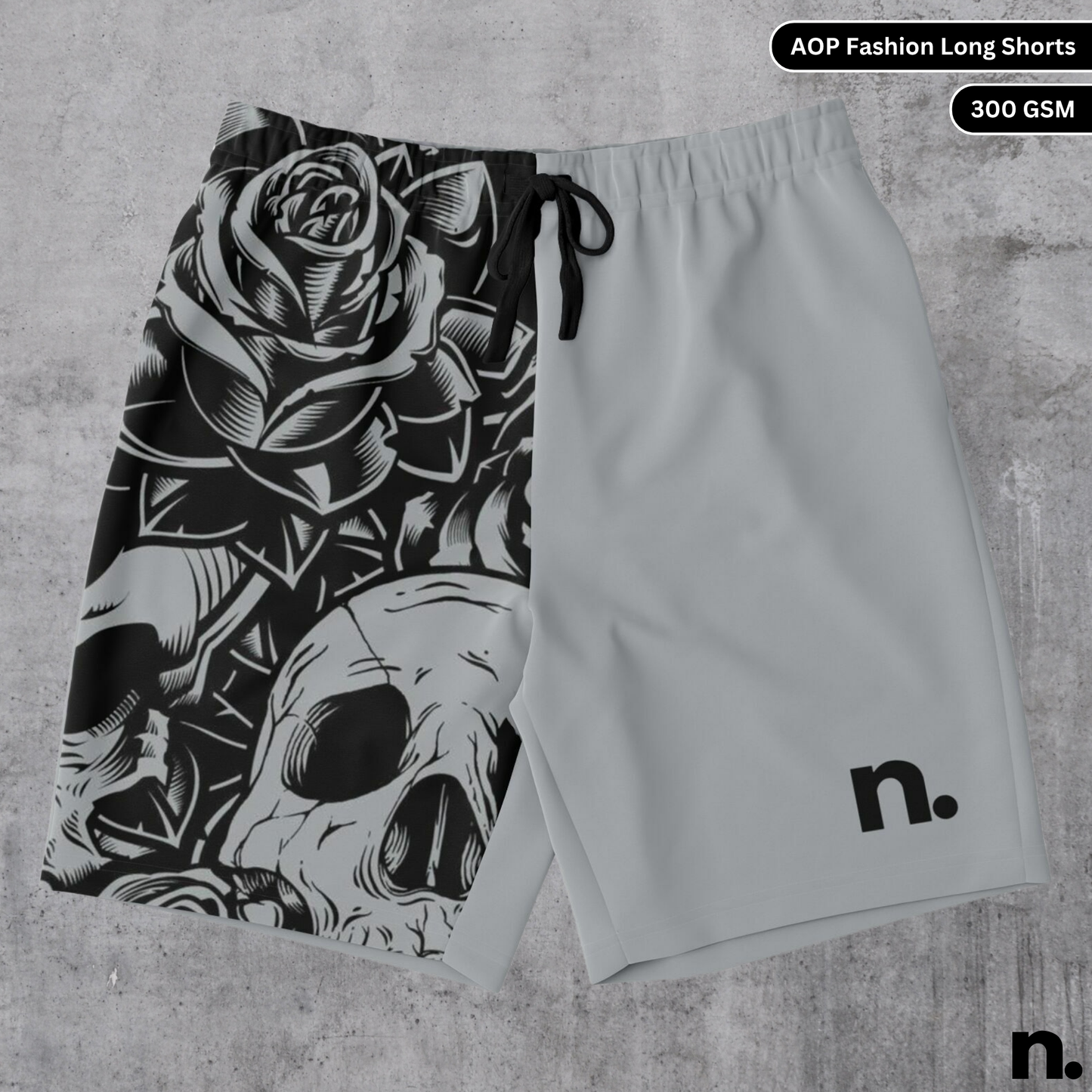 A flat lay of men's long shorts featuring a skulls and floral pattern on one leg and a brand logo on the other, showcasing the drawstring closure and pockets.