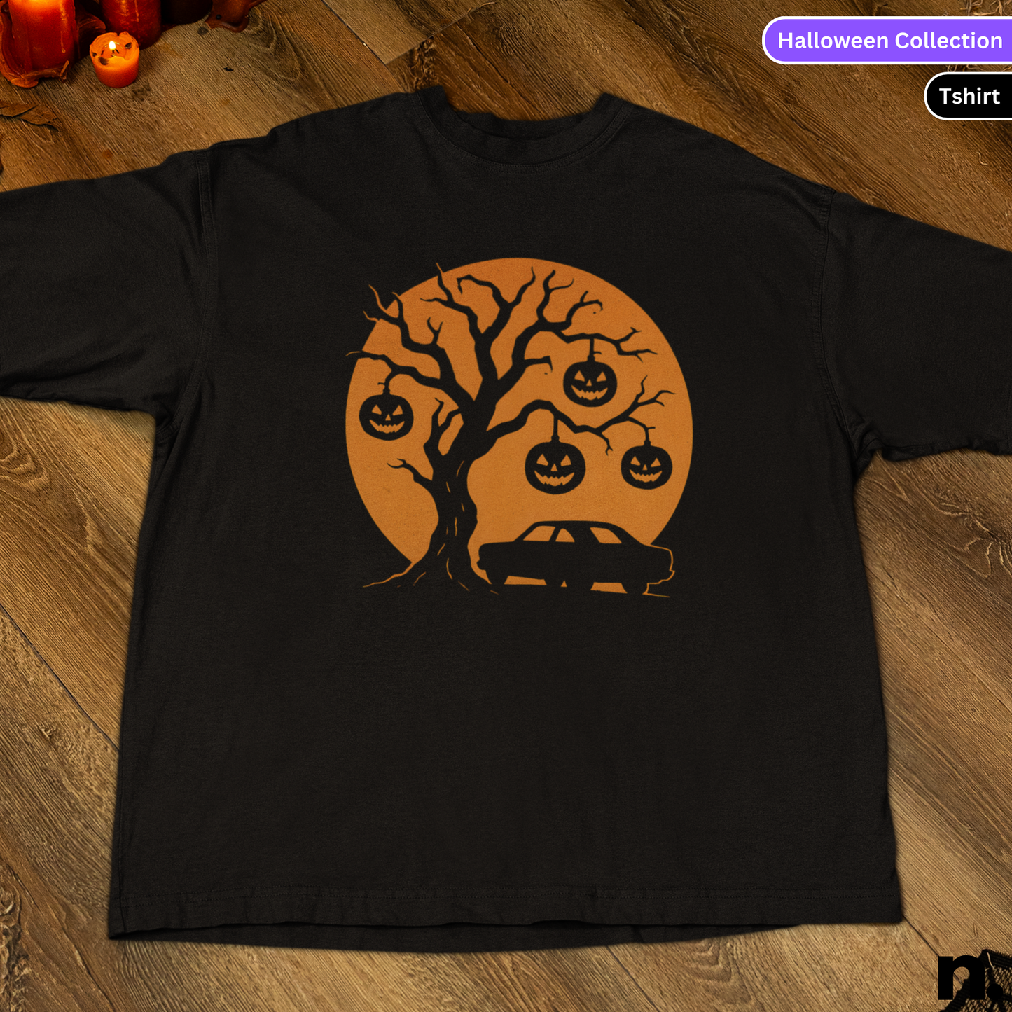 Black t-shirt with Halloween-themed design featuring a tree, pumpkins, and a car on a wooden surface.