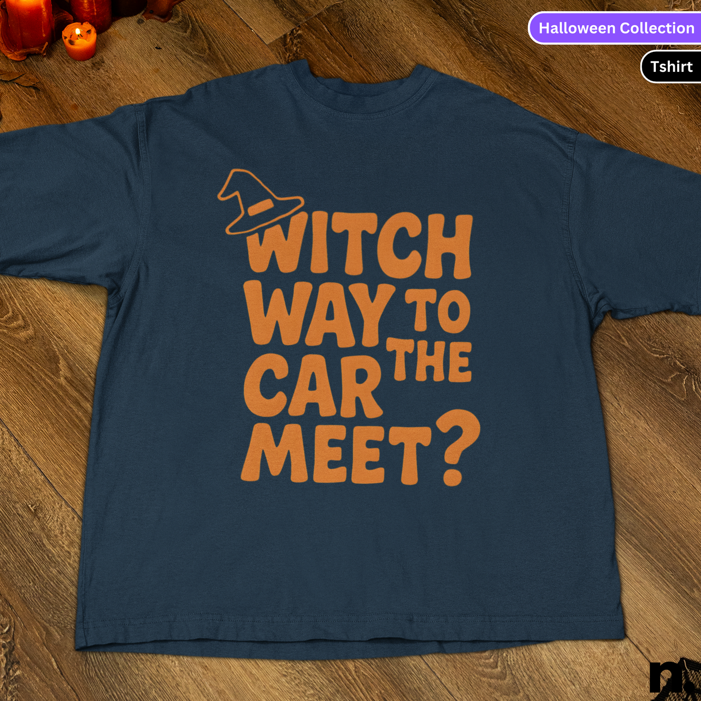 Blue t-shirt with orange text 'Witch way to the car meet?' on a wooden surface.