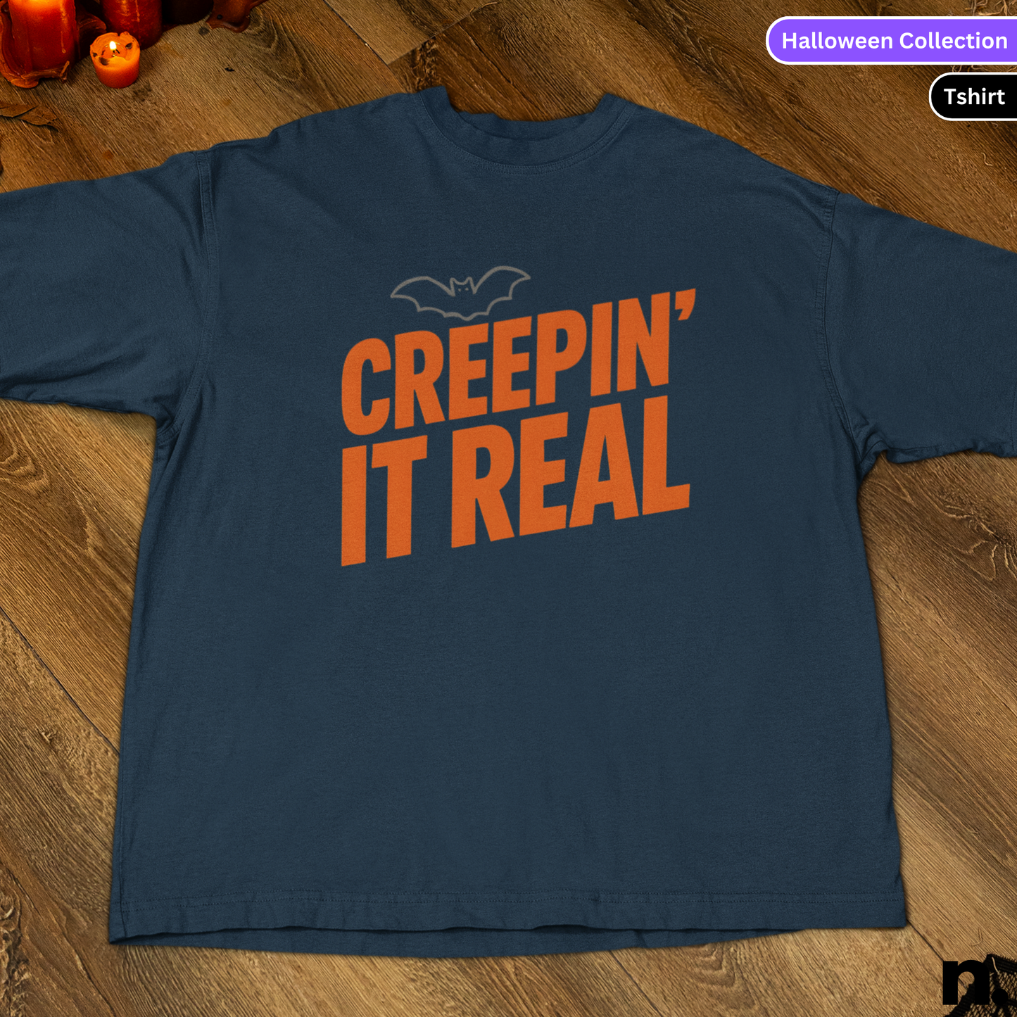 Navy blue t-shirt with orange text 'CREEPIN' IT REAL' on a wooden surface, part of a Halloween Collection.
