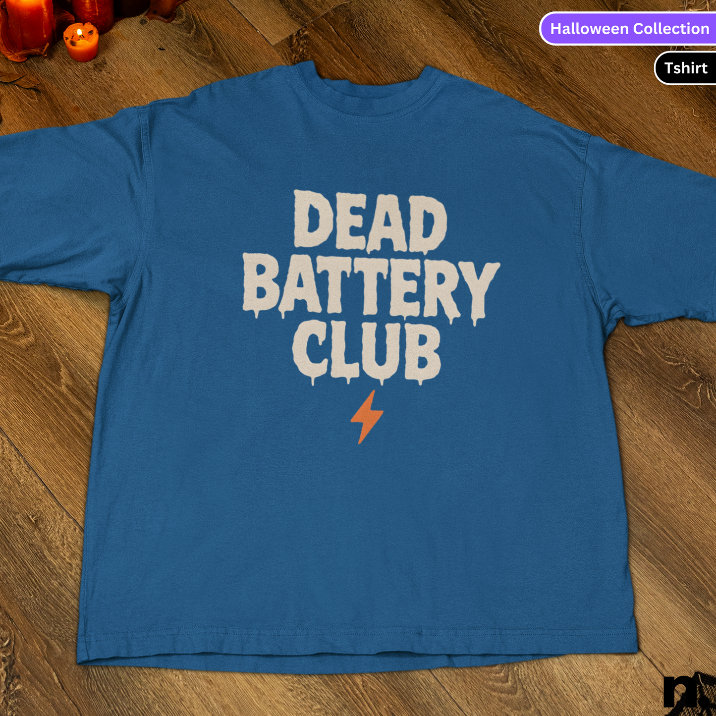 Blue t-shirt with 'DEAD BATTERY CLUB' text on a wooden floor