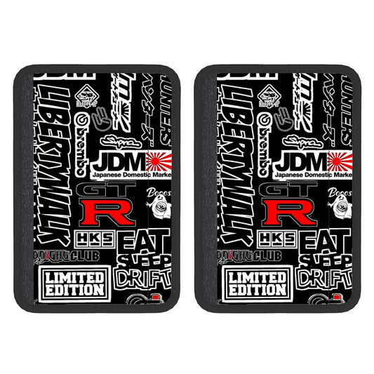 Two black neoprene seat belt cover pads with white text and graphics, including the terms 'JDM' and 'Limited Edition'. The pads are designed to be attached to a seat belt.