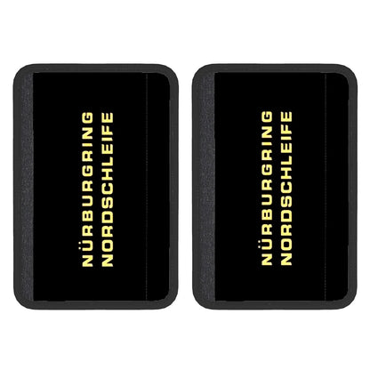 Two black neoprene seat belt cover pads with 'Nürburgring Nordschleife' text in yellow, indicating a racing track, suggesting the product is designed for use in car seat belts.