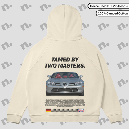Flat lay of full-zip hoodie featuring bold “TAMED BY TWO MASTERS.” car-inspired graphic, raglan sleeves, and fleece-lined interior in a clean, minimalist style.

