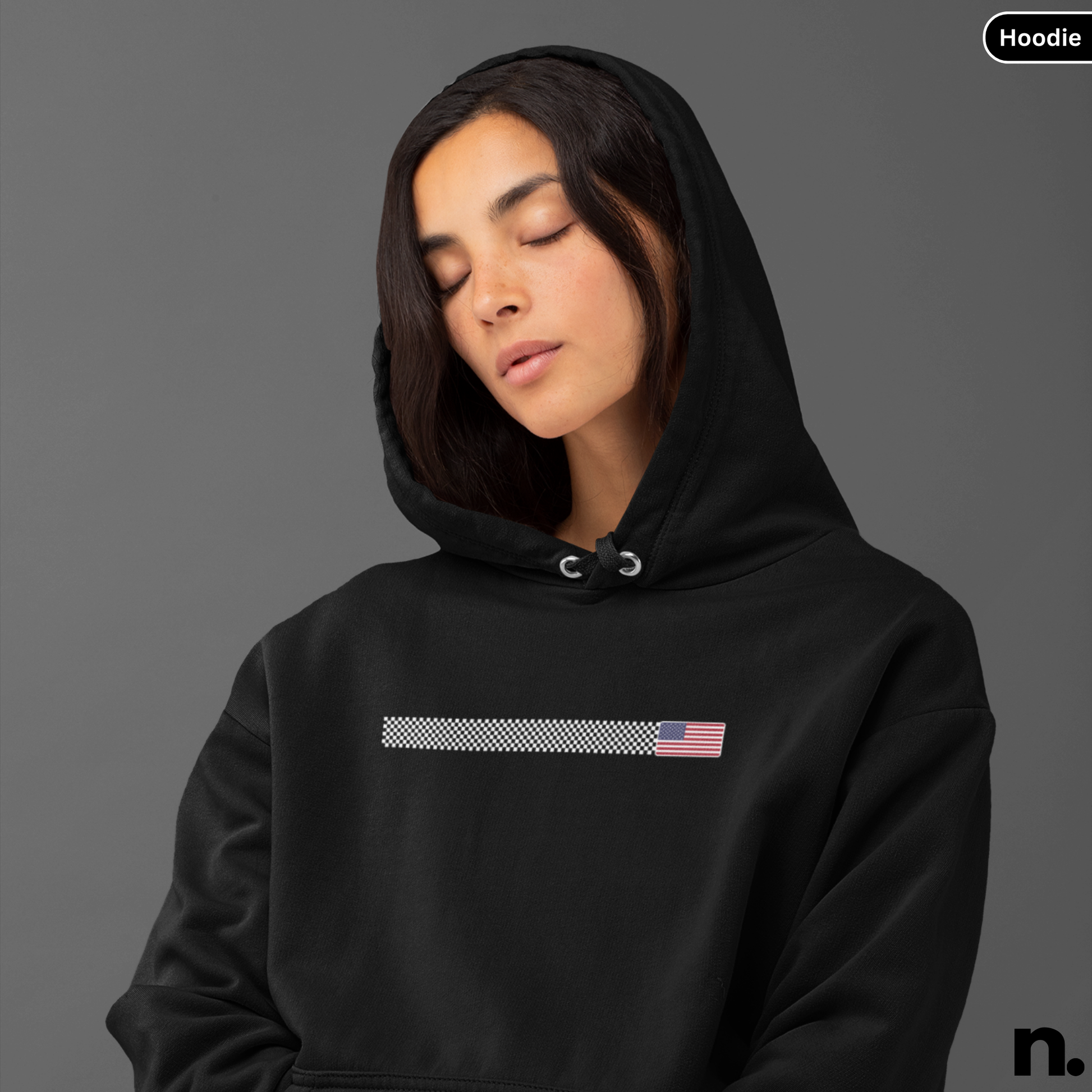 Person wearing a black hoodie with a small flag design on a gray background