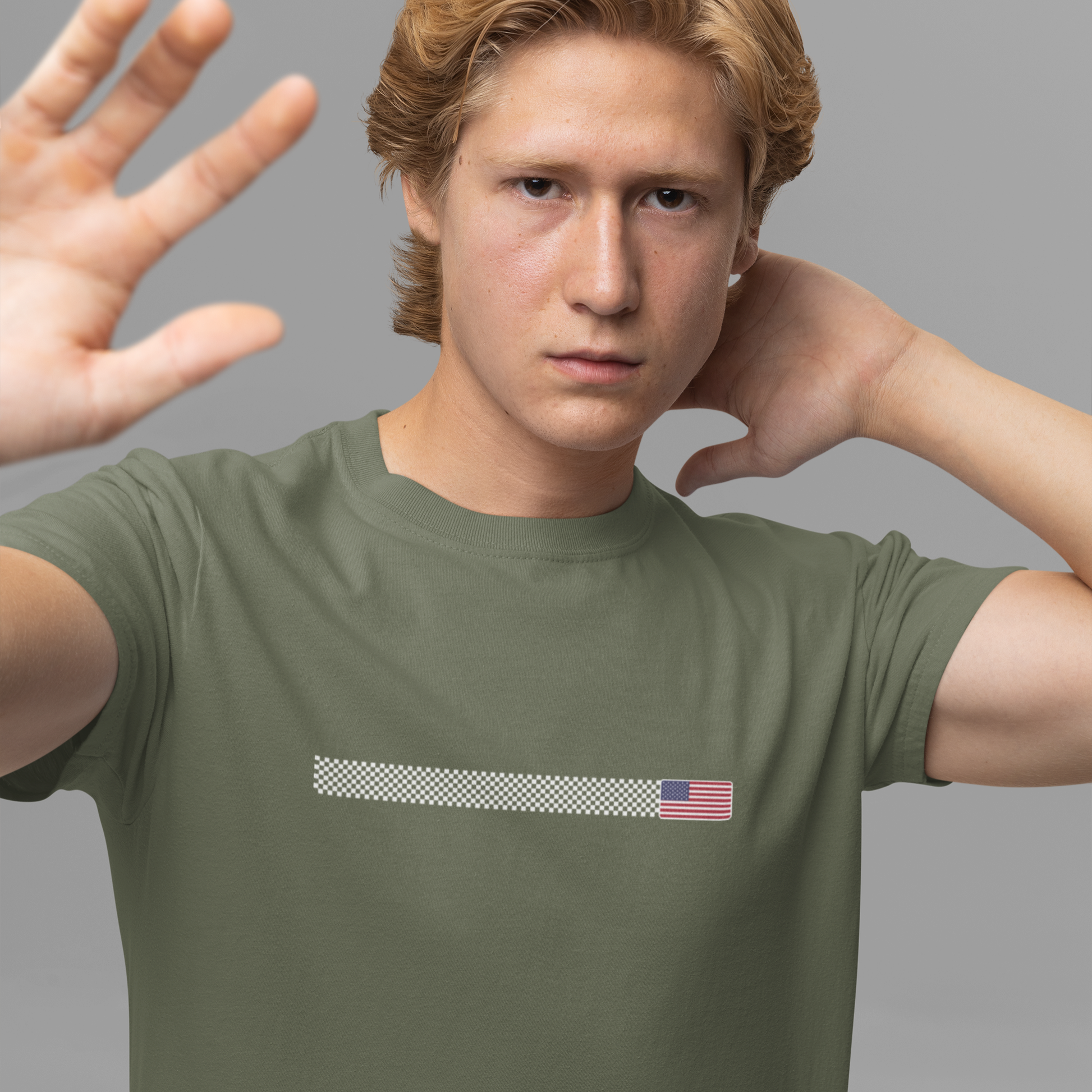Person wearing a green t-shirt with a small flag design on a gray background