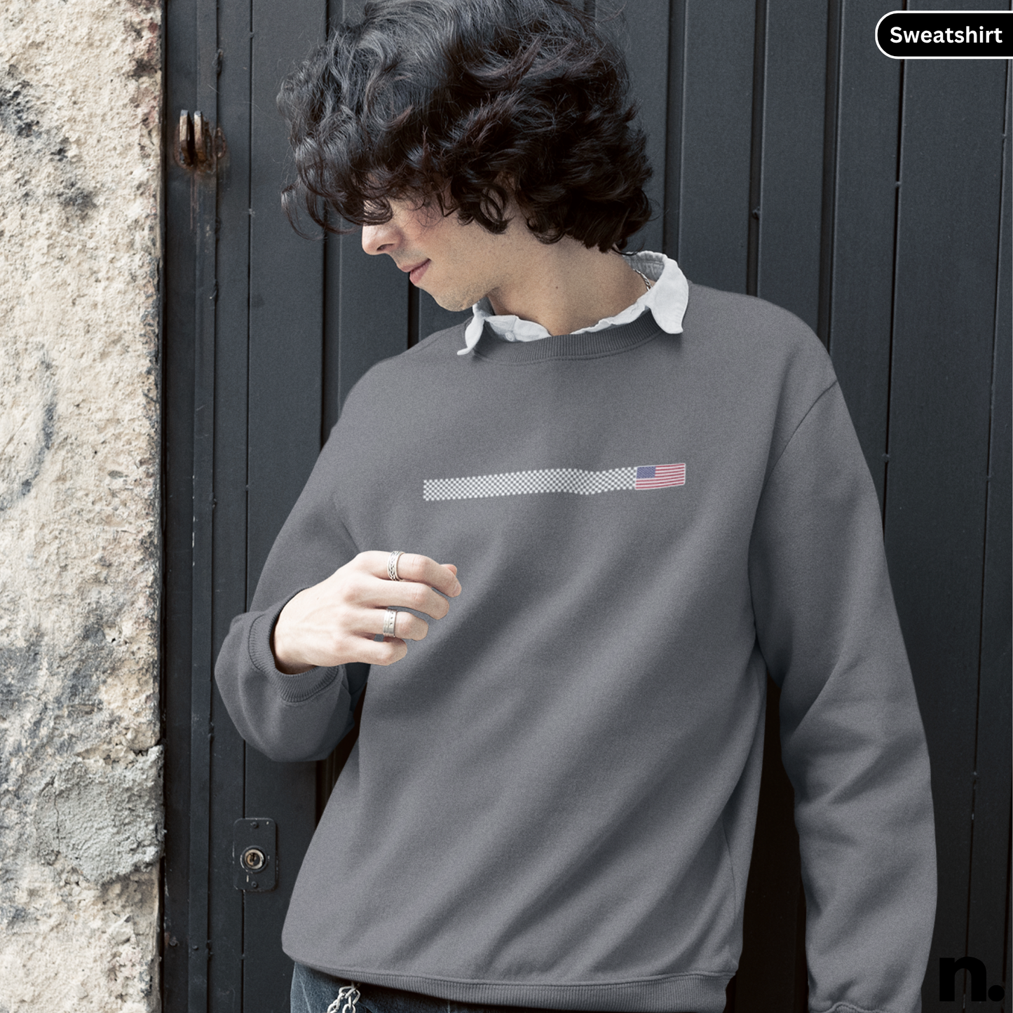 Person wearing a gray sweatshirt with a logo against a dark door and stone wall.