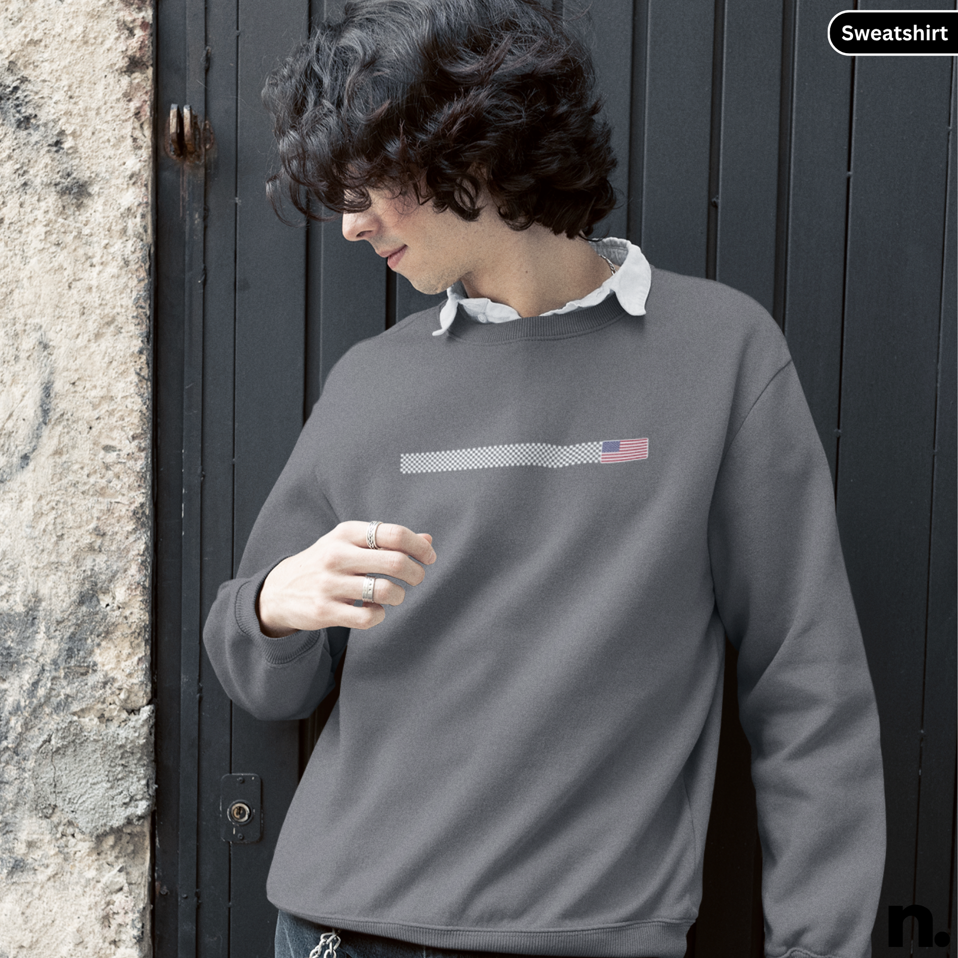 Person wearing a gray sweatshirt with a logo against a dark door and stone wall.