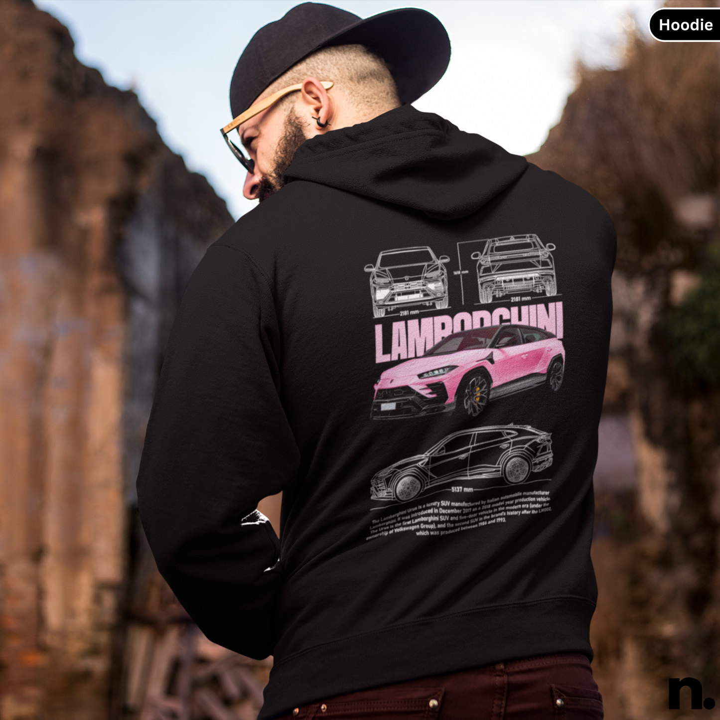 Person wearing a black hoodie with a graphic design of cars on the back, standing outdoors.