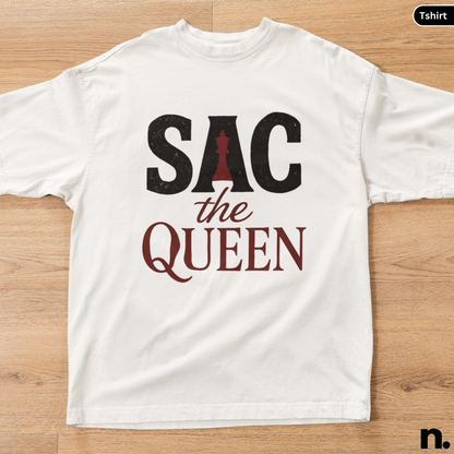White t-shirt with 'SAC the Queen' text and chess piece design on a wooden surface