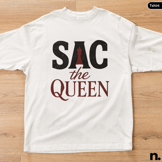 White t-shirt with 'SAC the Queen' text and chess piece design on a wooden surface