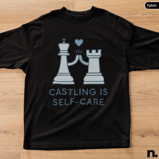 Black t-shirt with chess piece design and text 'CASTLING IS SELF-CARE' on a wooden surface.