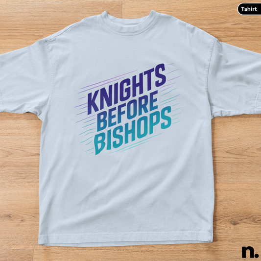 White t-shirt with 'Knights Before Bishops' text on a wooden surface
