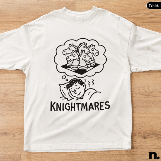 White t-shirt with black graphic design of a child dreaming about unicorns and the word 'Knightmares' on a wooden surface.