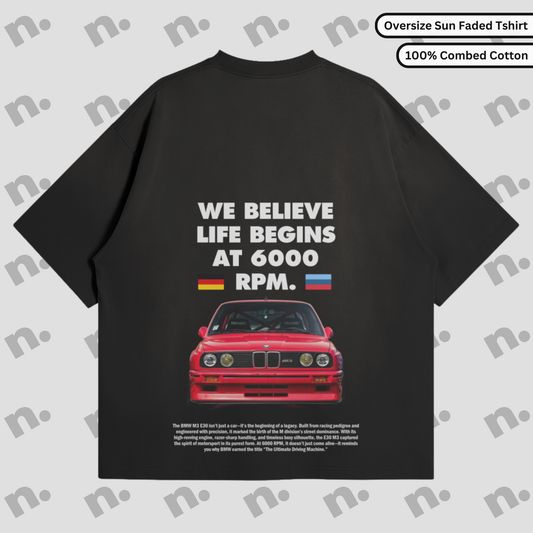 Flat lay of a dark-colored T-shirt featuring a minimalist BMW E30 inspired graphic, paired with modern streetwear accessories on a neutral background.
