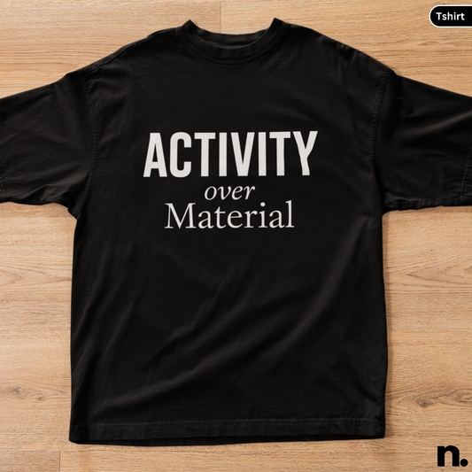 Black t-shirt with 'ACTIVITY over MATERIAL' text on a wooden surface