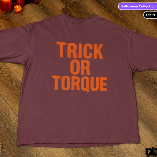 Purple t-shirt with 'TRICK OR TORQUE' text on a wooden surface, Halloween Collection label.
