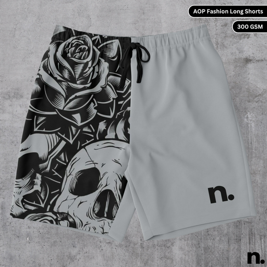 A flat lay of men's long shorts featuring a skulls and floral pattern on one leg and a brand logo on the other, showcasing the drawstring closure and pockets.