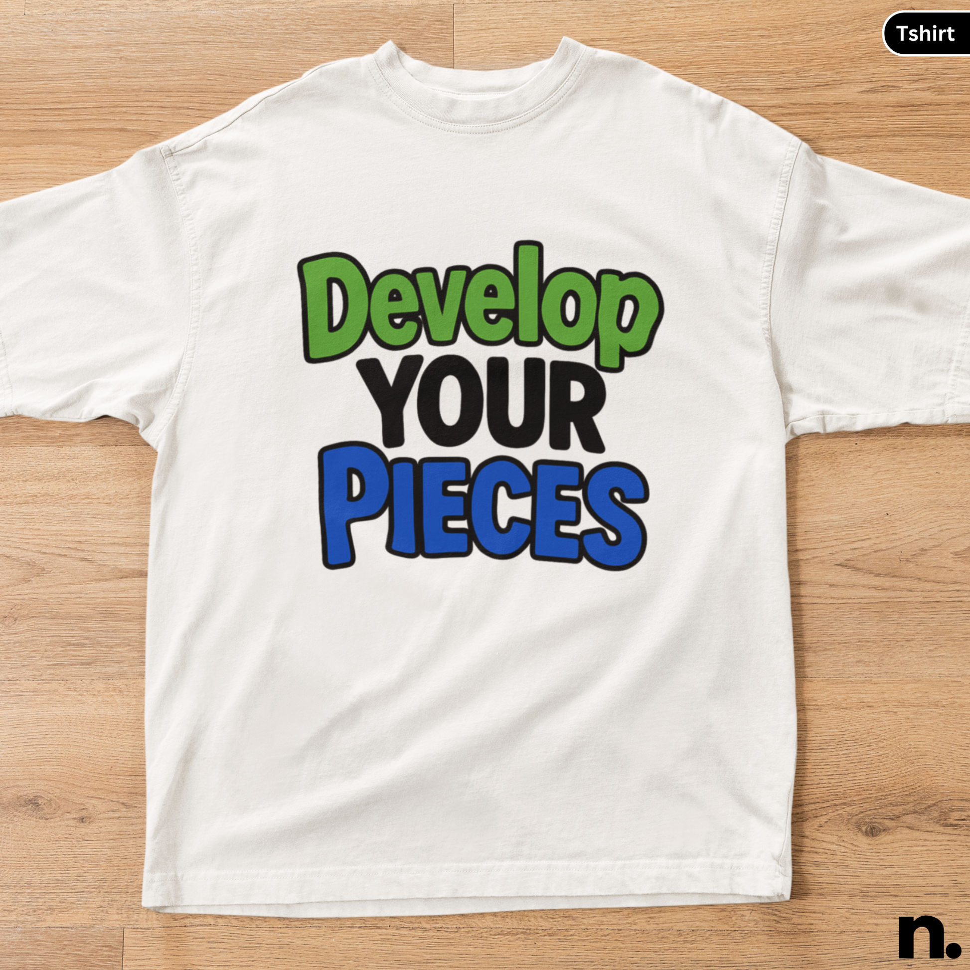 White t-shirt with colorful text 'Develop Your Pieces' on a wooden surface