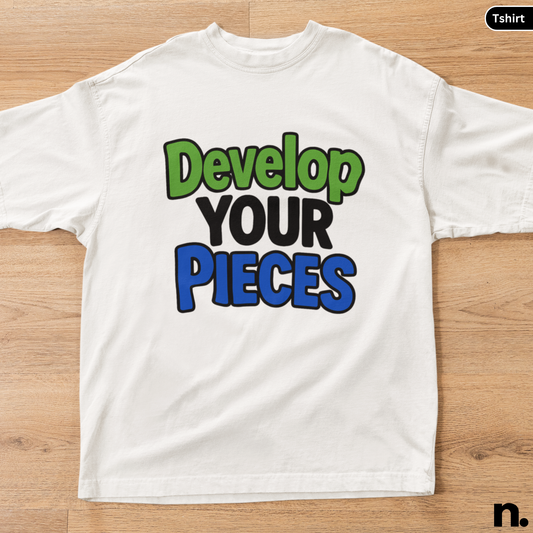White t-shirt with colorful text 'Develop Your Pieces' on a wooden surface