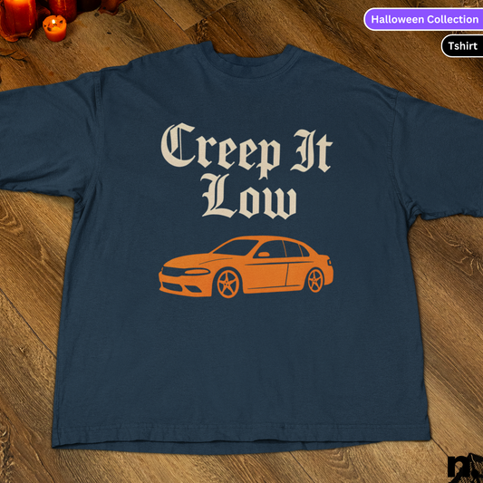 Navy blue t-shirt with 'Creep It Low' text and orange car graphic on a wooden surface.