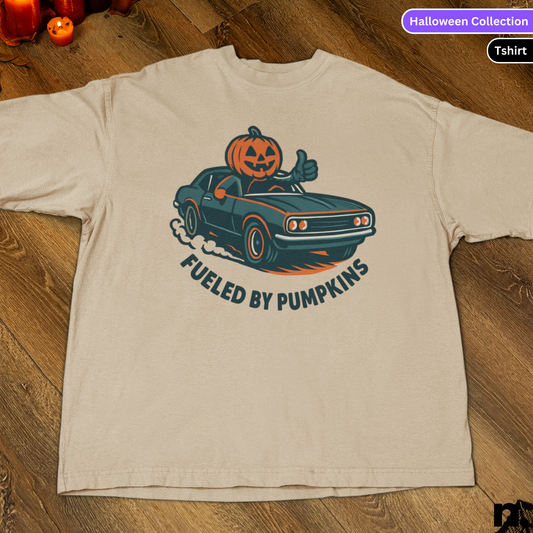 Beige t-shirt with a graphic of a car with a pumpkin on top and 'Fueled by Pumpkins' text, on a wooden surface.