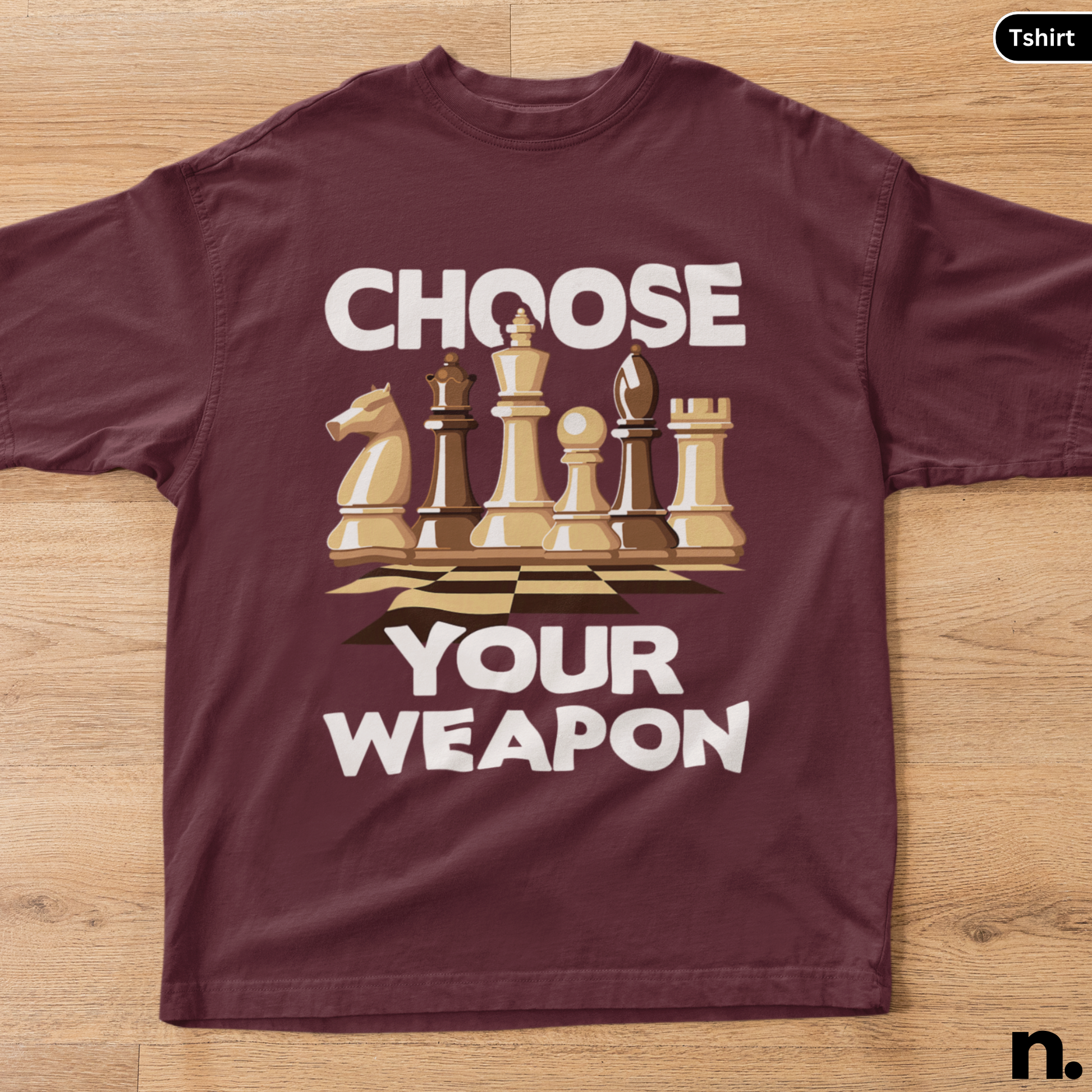 Maroon t-shirt with chess piece graphic and text 'Choose Your Weapon' on a wooden surface