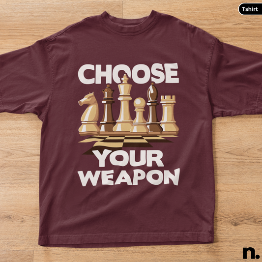 Maroon t-shirt with chess piece graphic and text 'Choose Your Weapon' on a wooden surface