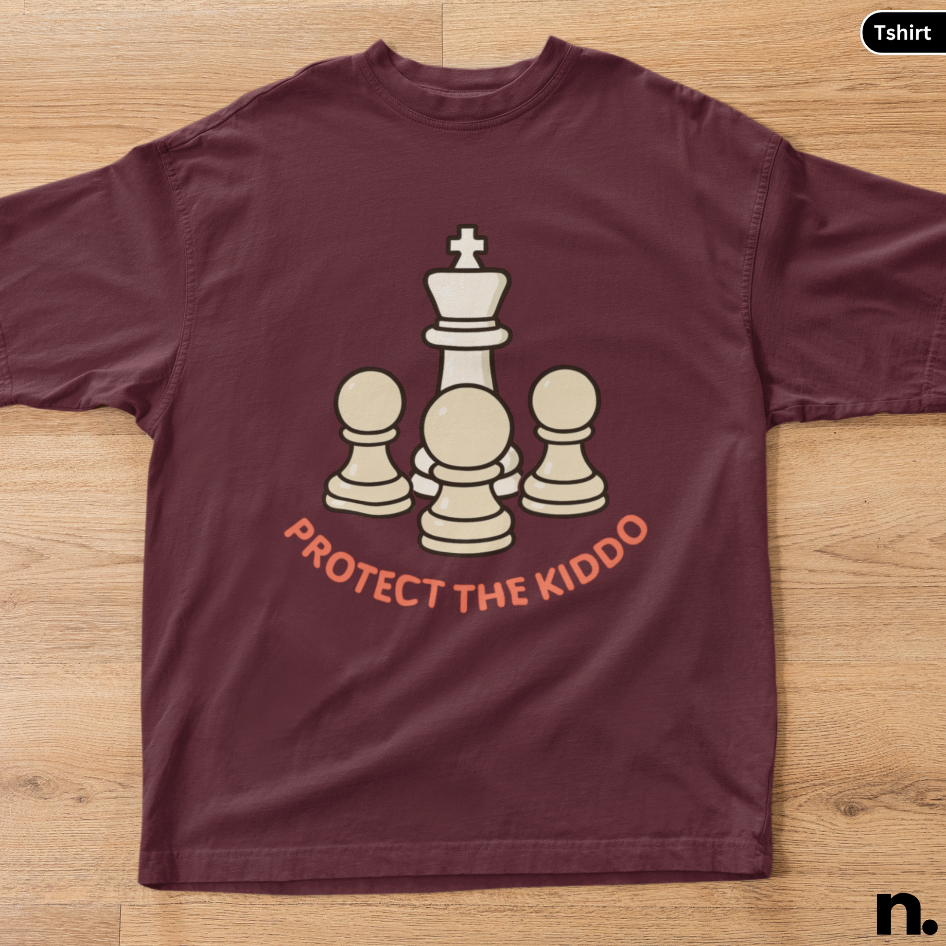 Maroon t-shirt with chess piece design and 'Protect the Kiddo' text on a wooden surface