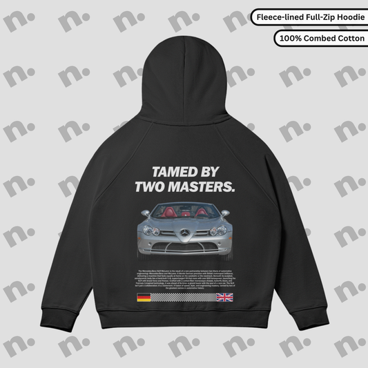 Flat lay of full-zip hoodie featuring bold “TAMED BY TWO MASTERS.” car-inspired graphic, raglan sleeves, and fleece-lined interior in a clean, minimalist style.

