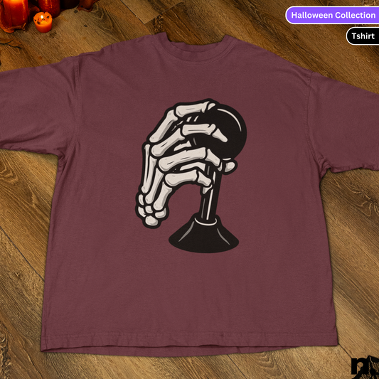 Maroon t-shirt with skeleton hand design on a wooden surface, labeled 'Halloween Collection'.