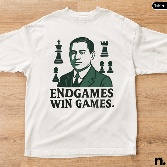 White t-shirt with a graphic of a man in a suit and chess pieces, featuring the text 'ENDGAMES WIN GAMES.' on a wooden surface.