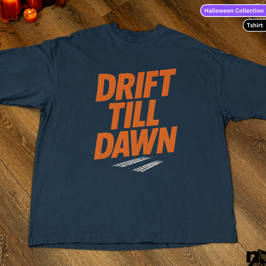 Navy blue t-shirt with 'DRIFT TILL DAWN' text in orange on a wooden surface.
