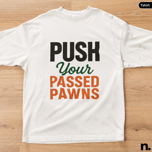 White t-shirt with text 'Push Your Passed Pawns' on a wooden surface