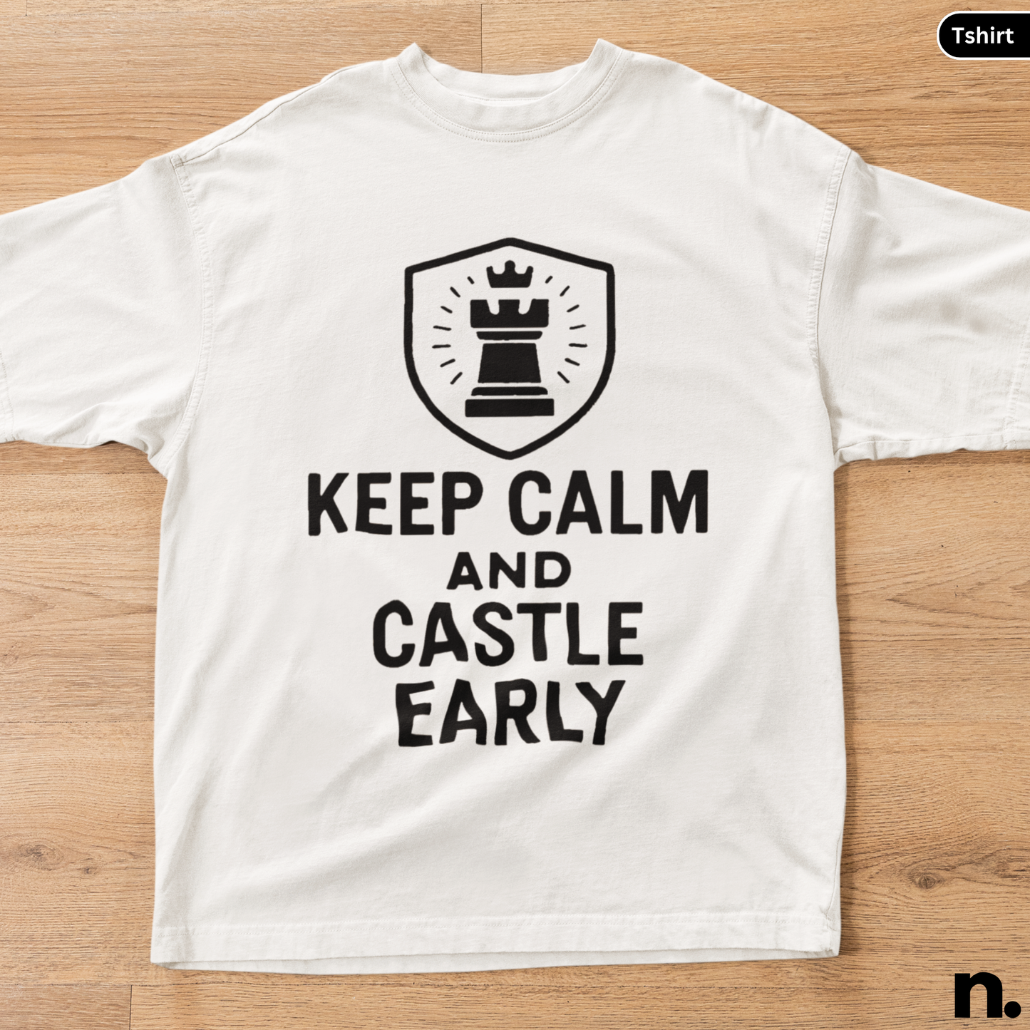 White t-shirt with a black chess-themed design on a wooden surface