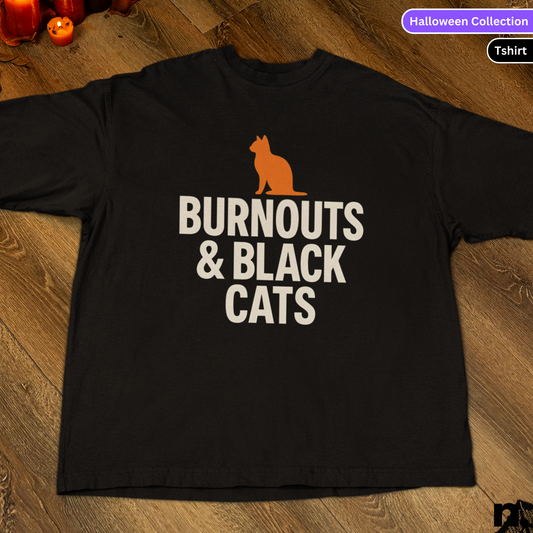 Black t-shirt with 'Burnouts & Black Cats' text and orange cat graphic on a wooden surface.