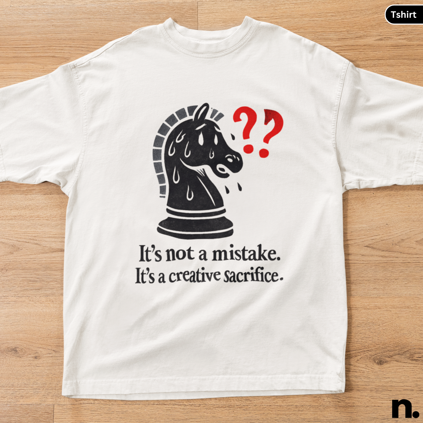 White t-shirt with a black chess piece graphic and text on a wooden surface