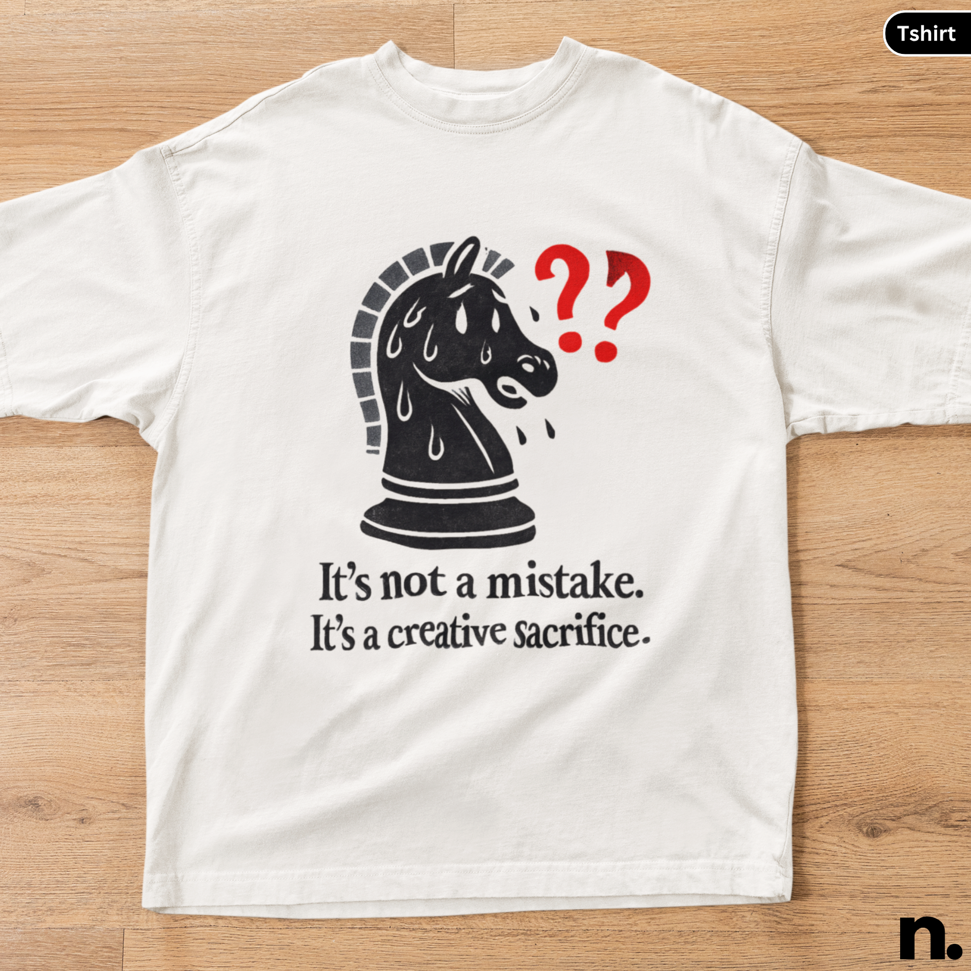White t-shirt with a black chess piece graphic and text on a wooden surface