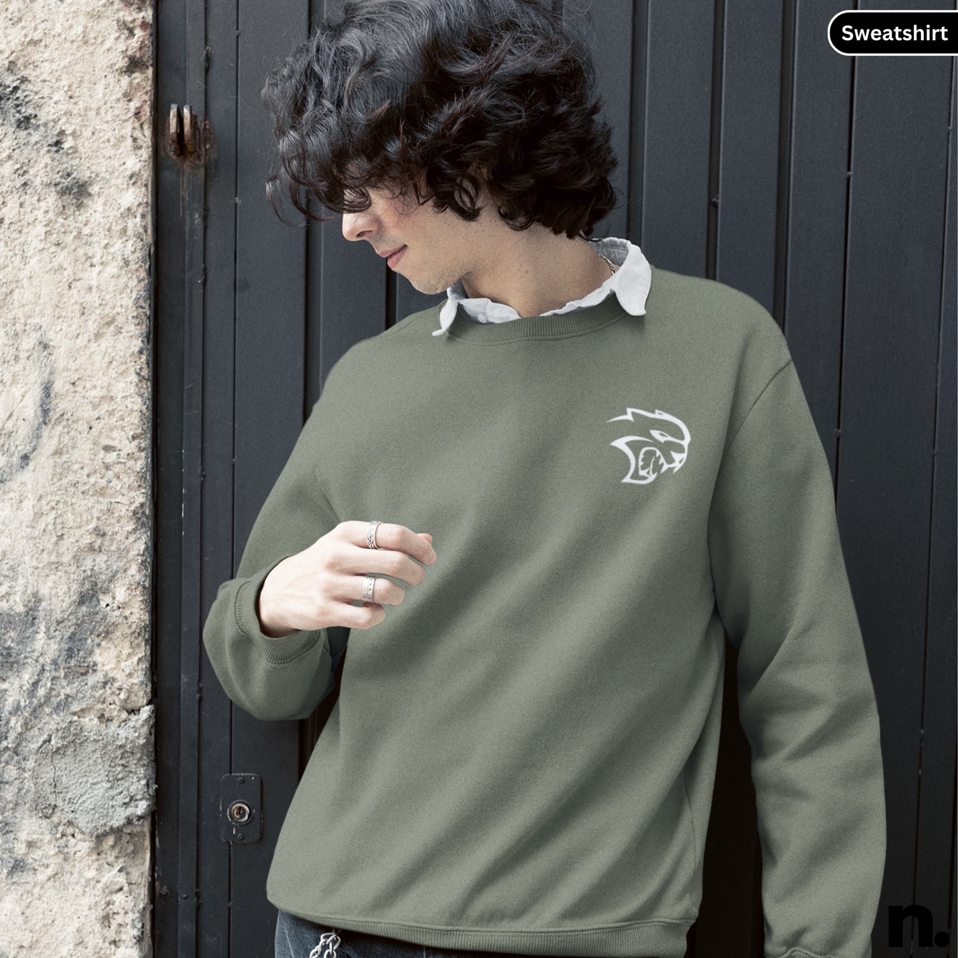 Person wearing a green sweatshirt with a logo, standing against a dark door.