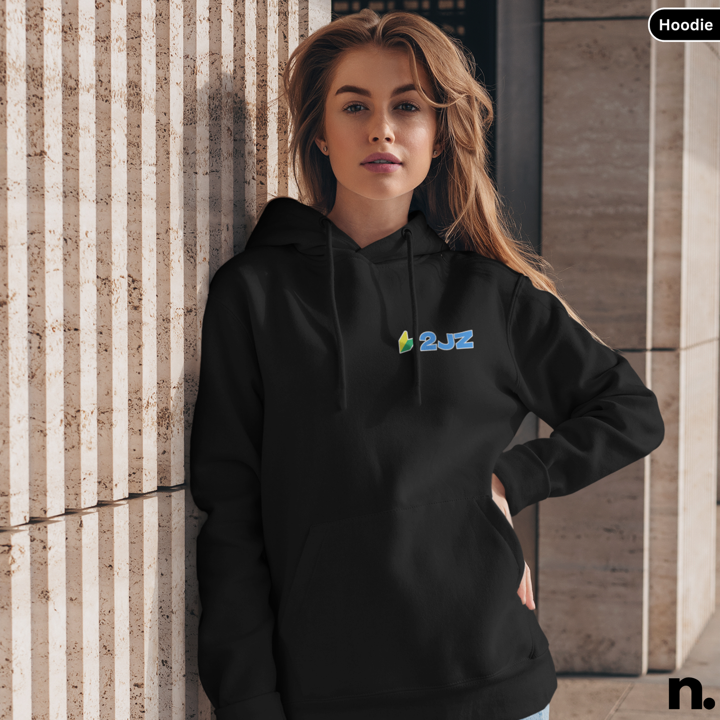 Woman wearing a black hoodie with a logo against a textured wall.