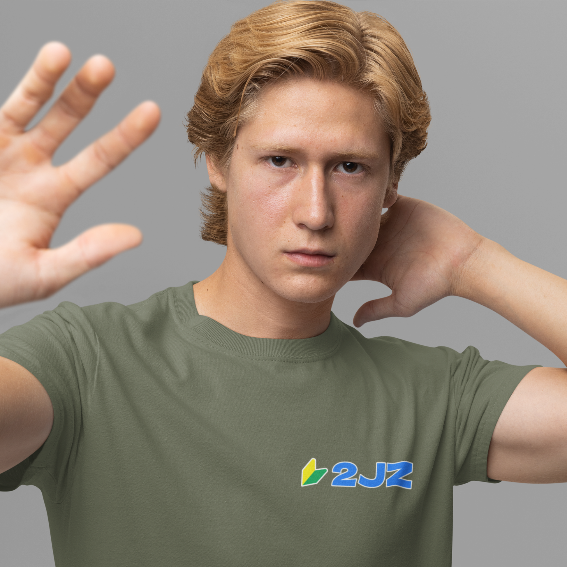 Person wearing a green t-shirt with a logo, making a gesture with their hands.