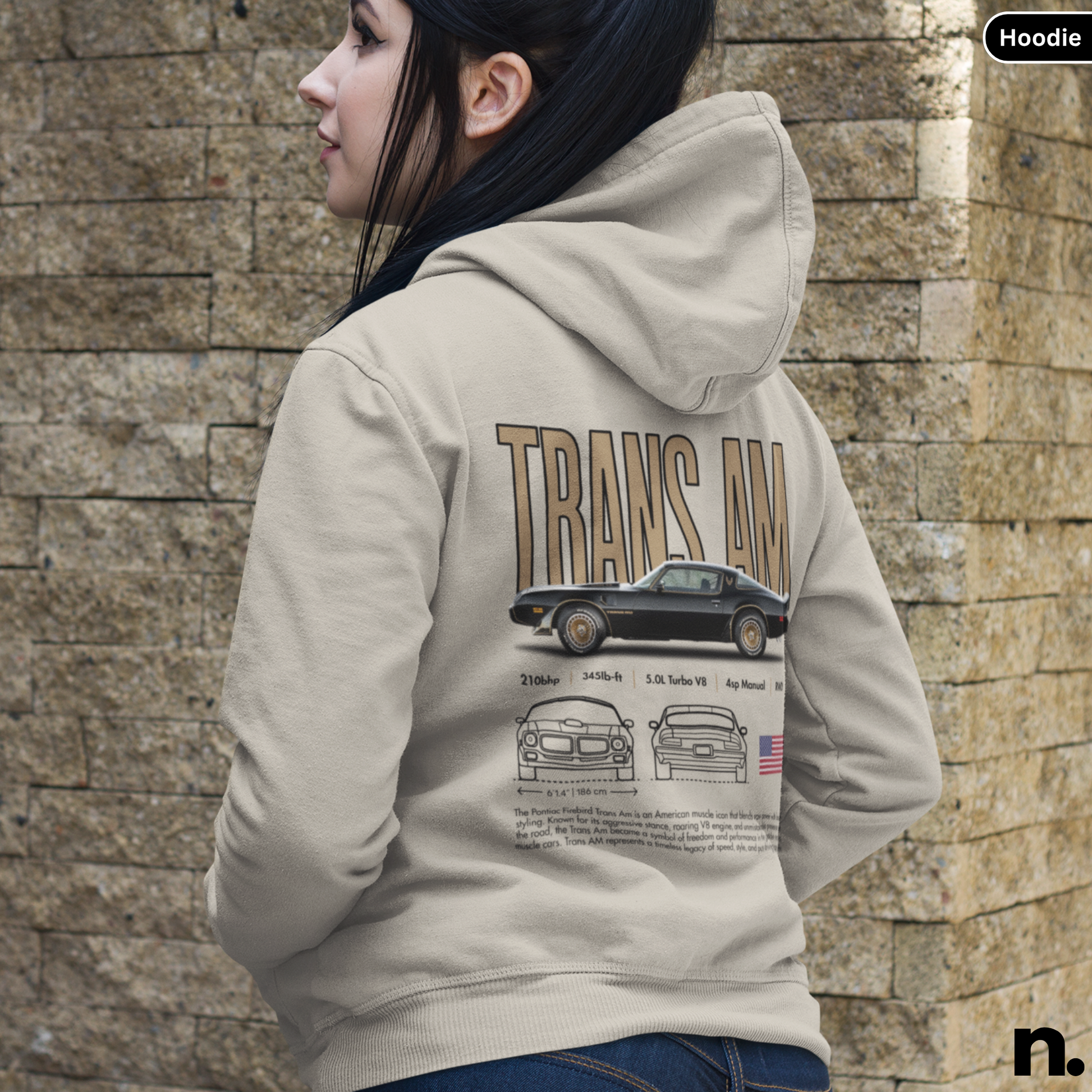 Person wearing a hoodie with 'Trans Am' design on the back against a stone wall.
