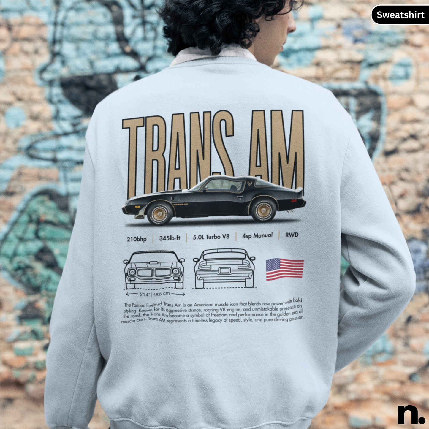 Person wearing a sweatshirt with a graphic of a car and text on the back, against a graffiti-covered wall.