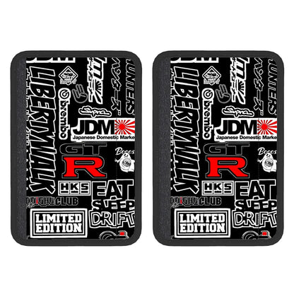 Two black neoprene seat belt cover pads with white text and graphics, including the terms 'JDM' and 'Limited Edition'. The pads are designed to be attached to a seat belt.